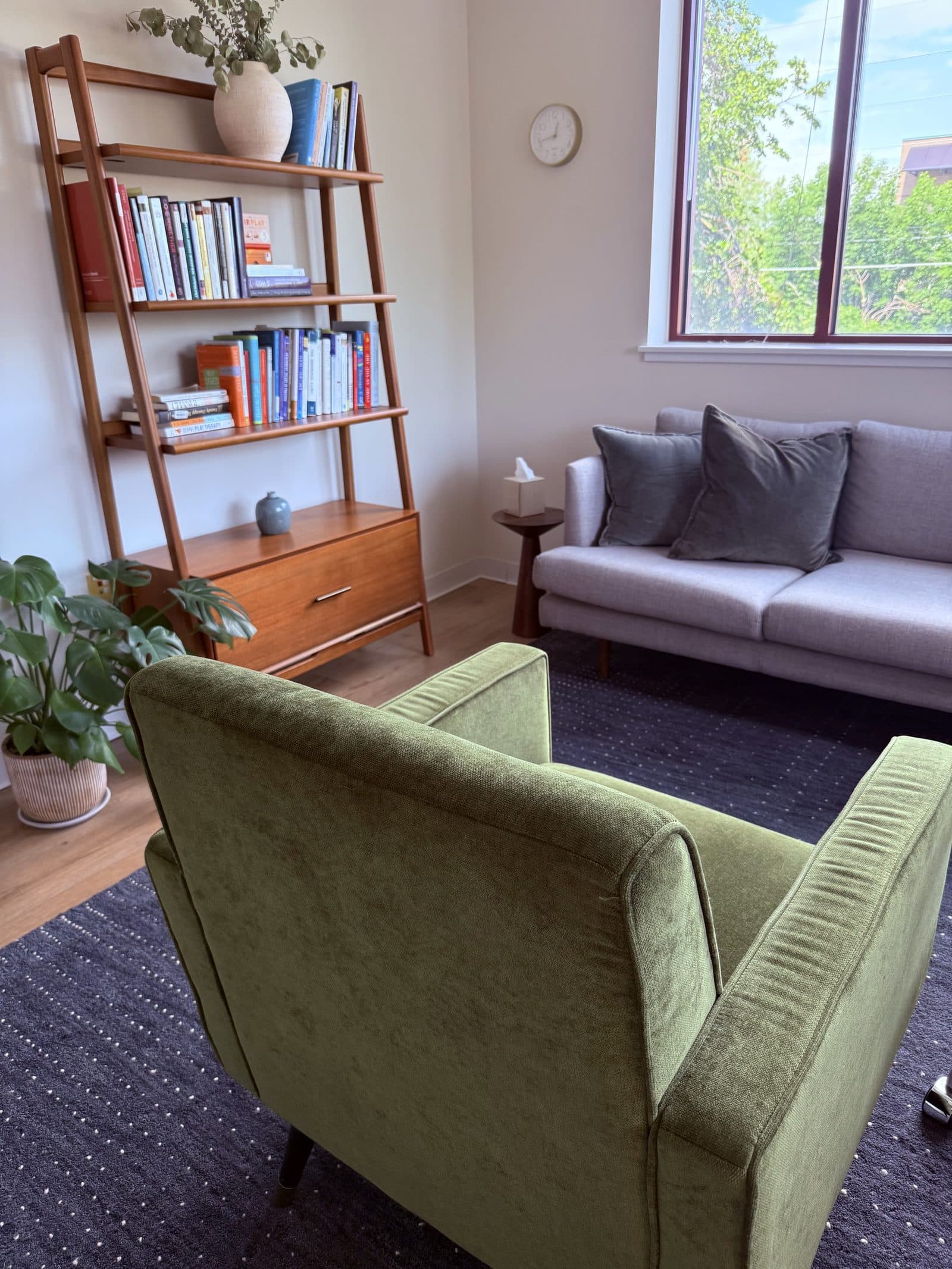 A therapy room at Flatirons Relationship Center in Boulder, CO, with a bookshelf, armchairs, and a couch beside the window